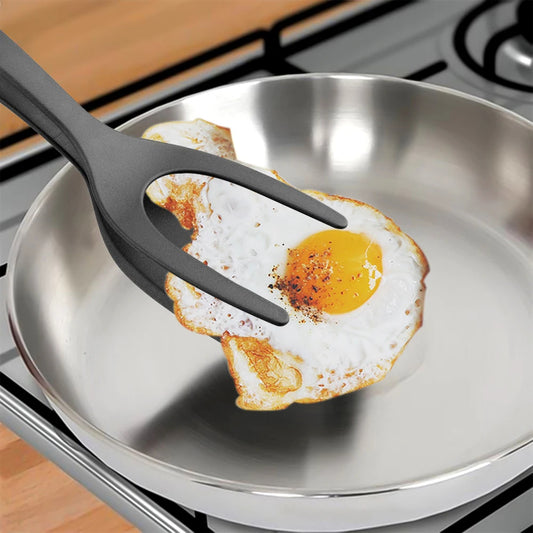 Fried egg on a metal pan with a black utensil, on a stove.