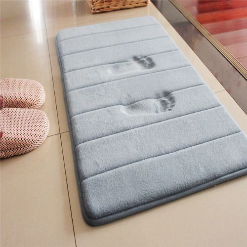 Gray bath mat with footprints on a tiled floor next to pink slippers.
